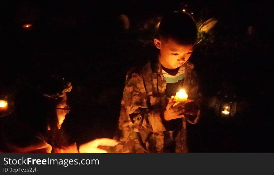 Boy holding candle in dark during indoor ceremony. Boy holding candle in dark during indoor ceremony.