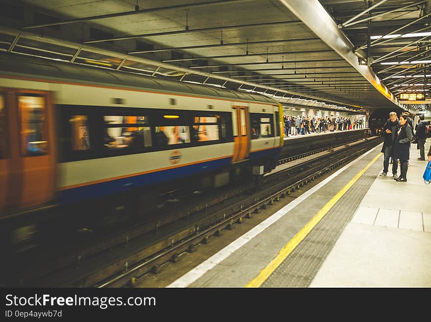 Travelers on platform with train moving along rails in underground station. Travelers on platform with train moving along rails in underground station.