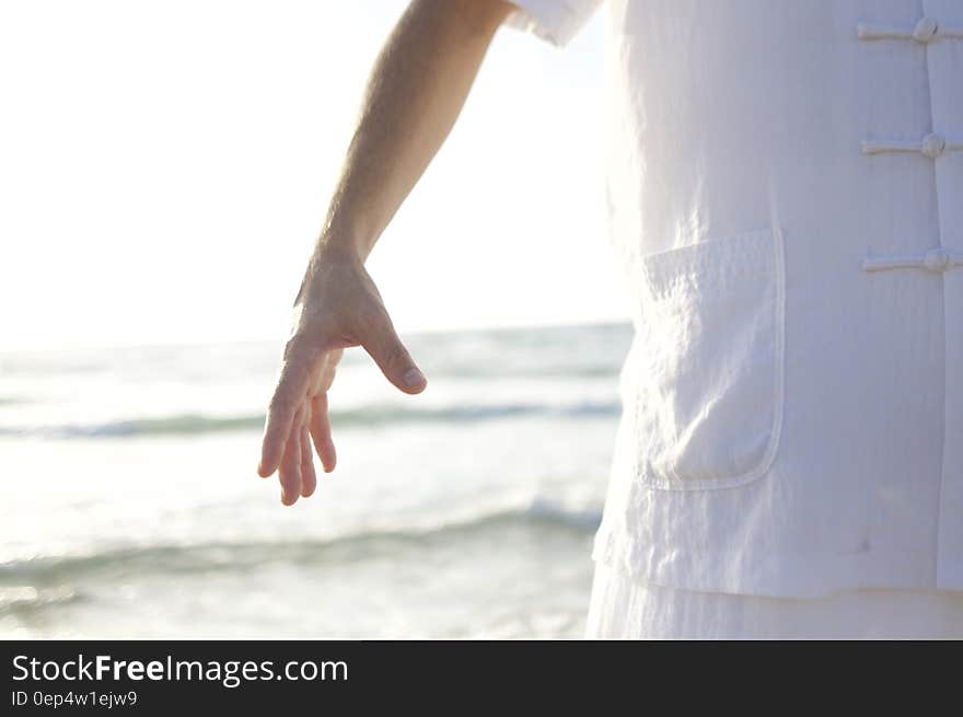 Person in White Shirt Standing on Seashore during Daytime