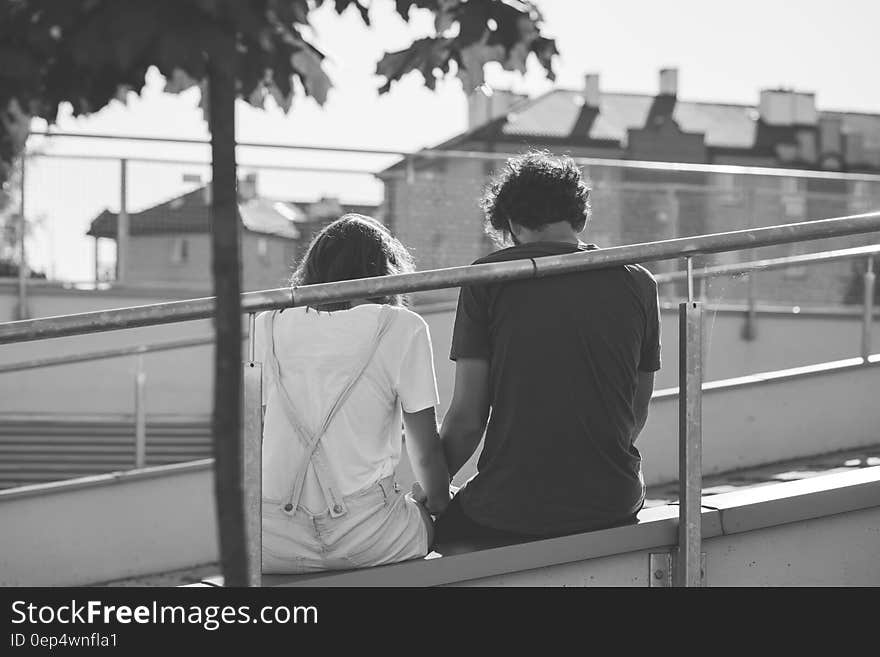 Grayscale Photo of Man and Woman Sitting on Inclined Road