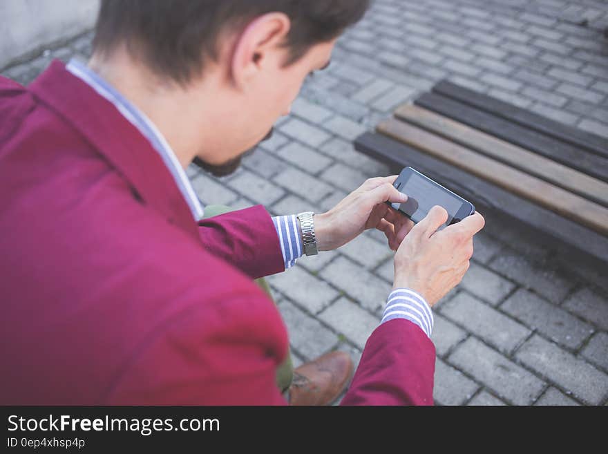 Man in Magenta Suit Jacket Holding Smartphone With Both Hands