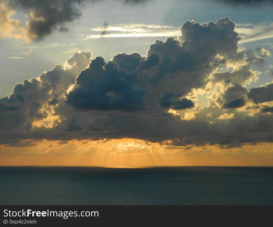 Sun Behind the White Clouds Above Body of Water during Daytime
