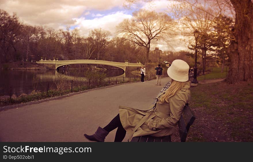 Woman in White Bucket Hat, Brown Coat and Boots Sitting on Bench at Park