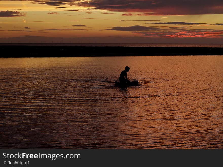 Silhouette of Person on Body of Water during Sunset