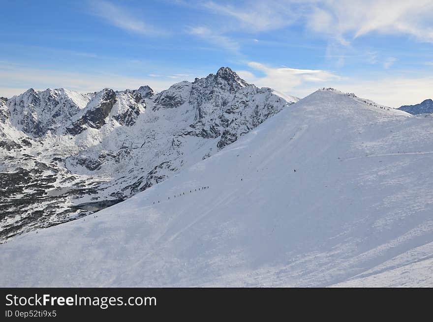 Alpine hikers from a distance climbing snow covered peak on sunny day. Alpine hikers from a distance climbing snow covered peak on sunny day.