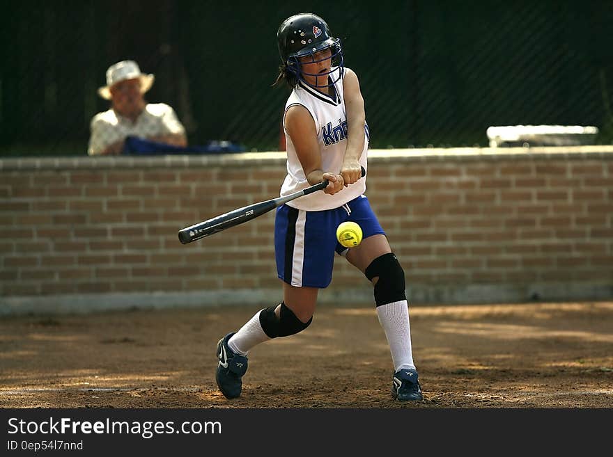 Woman in White Sleeveless Jersey Holding a Black Baseball Bat Pitching the Green Tennis Ball