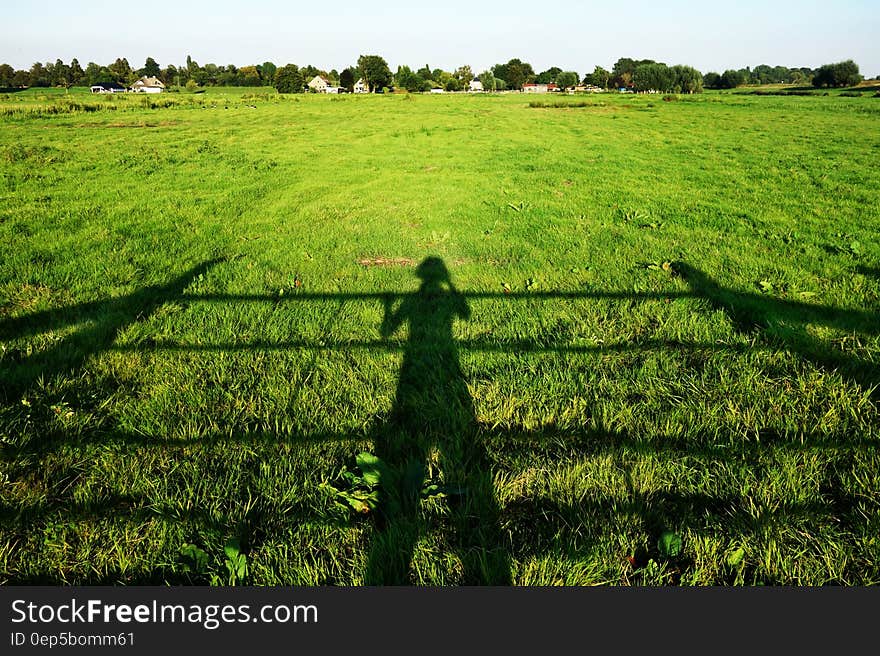 Shadow of a farmer looking inspecting his crop from a farm gate which leads into a pasture field with cottages situated at the far end of the field. Shadow of a farmer looking inspecting his crop from a farm gate which leads into a pasture field with cottages situated at the far end of the field.