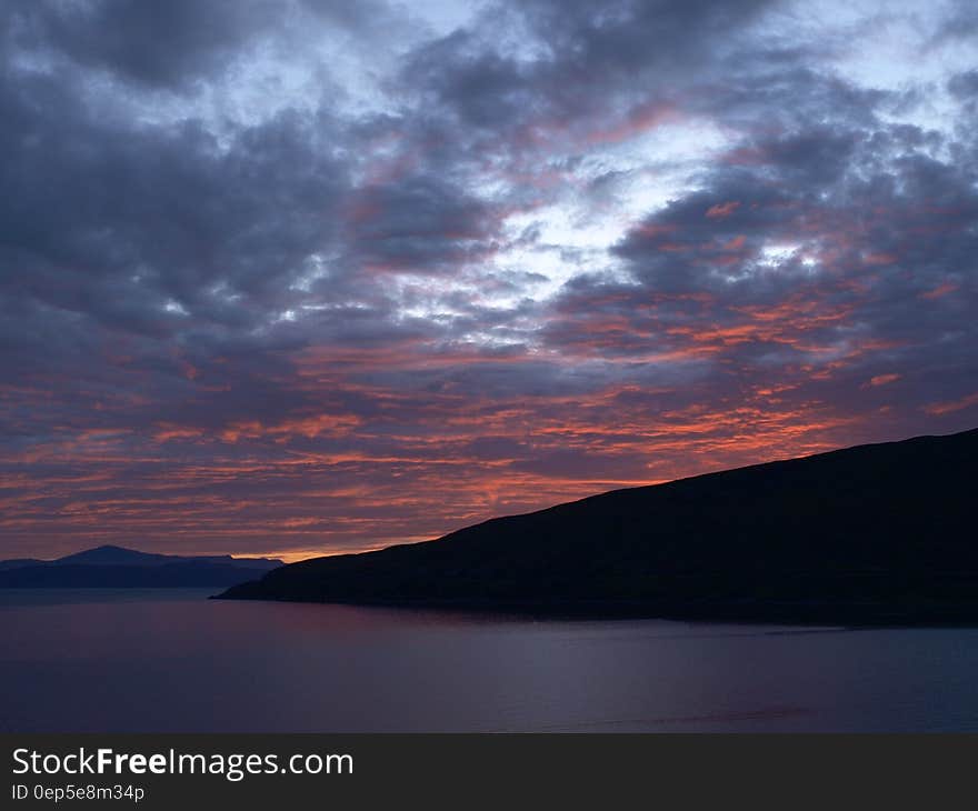 Landscape Photography of Black Rocky Formation With Orange Horizon Under Blue Clouds