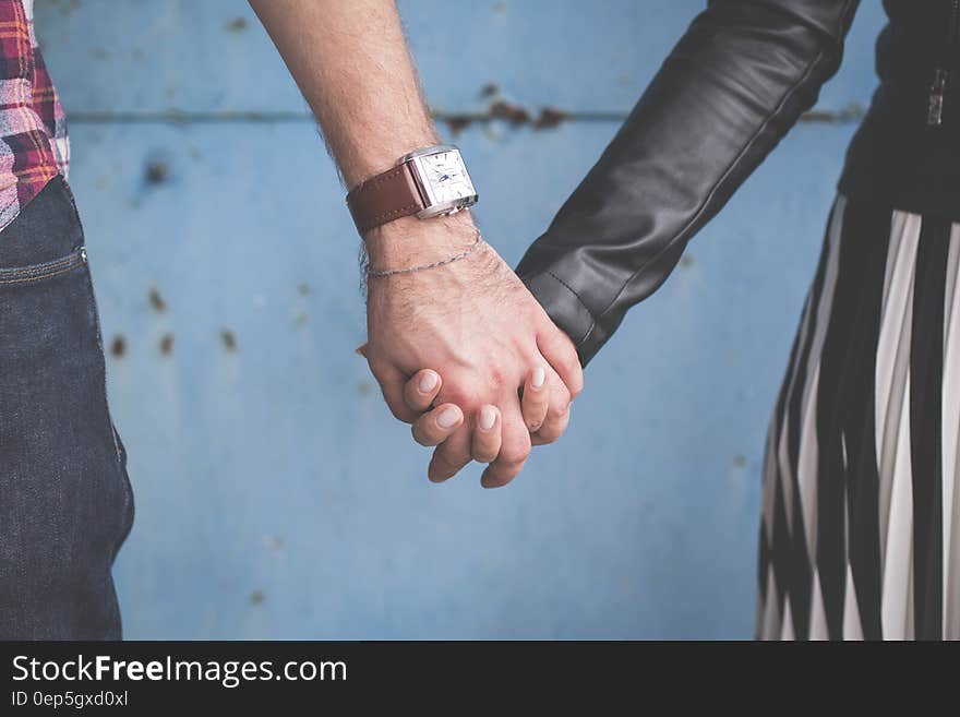 2 Person Holding Hands Besides Blue Painted Wall