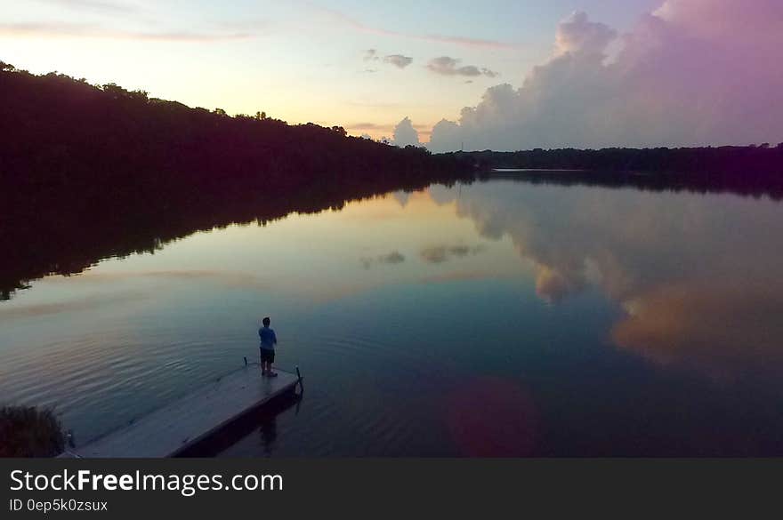 Man Standing on River Dock during Sunset