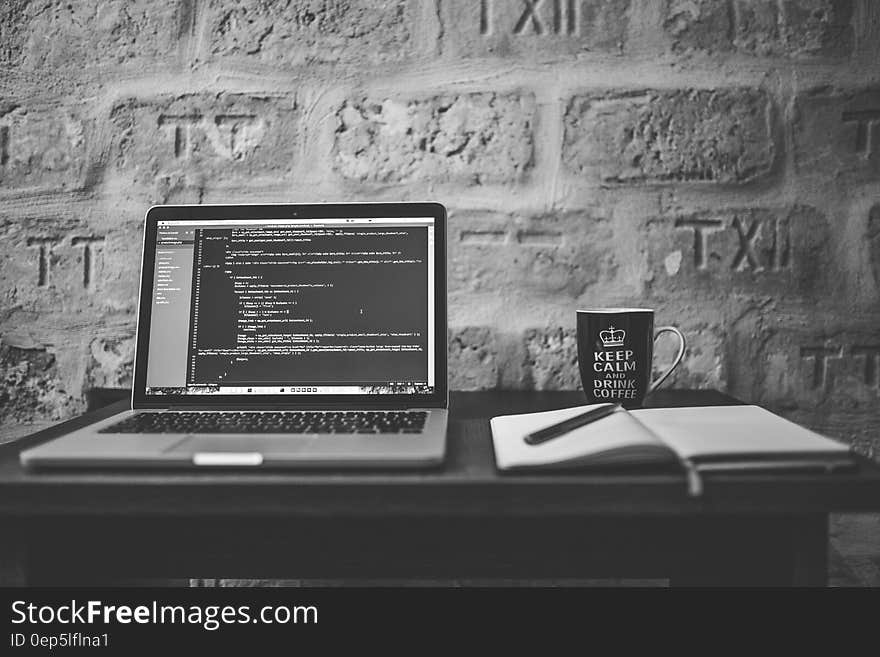 Grayscale Photo of Computer Laptop Near White Notebook and Ceramic Mug on Table