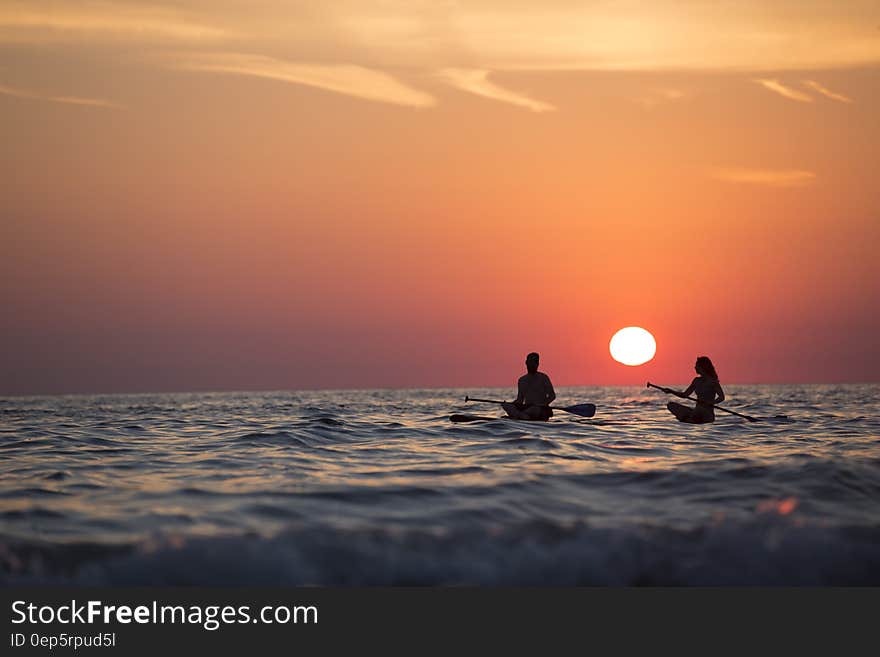 Man and Woman Boat Rowing in Sea during Golden Hour