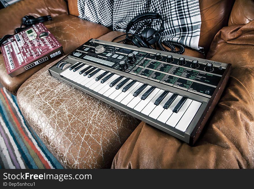 A keyboard synthesizer and a mixer on a vintage leather couch. A keyboard synthesizer and a mixer on a vintage leather couch.