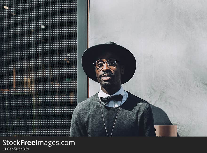 A black man with large-rimmed hat, eyeglasses and a bowtie standing against a concrete wall. A black man with large-rimmed hat, eyeglasses and a bowtie standing against a concrete wall.