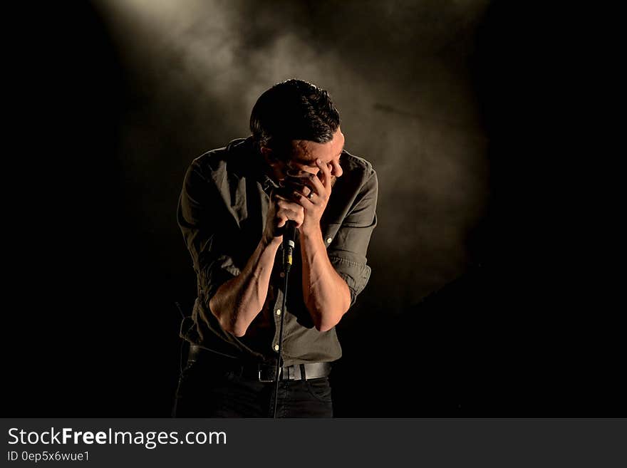 Man in Gray Dress Shirt Holding Mic in Dark Room