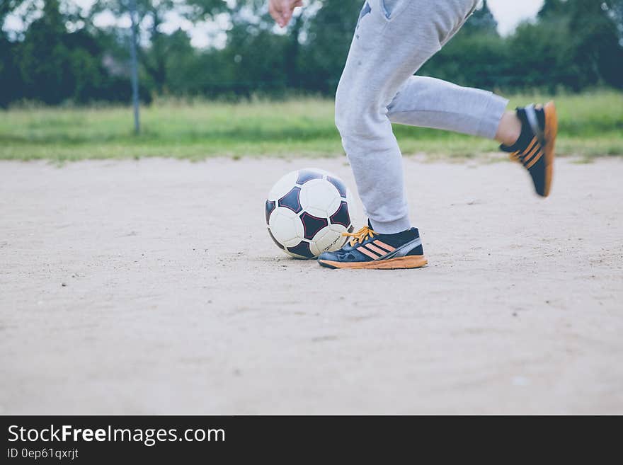 Person Kicking Soccer Ball on Gray Sand