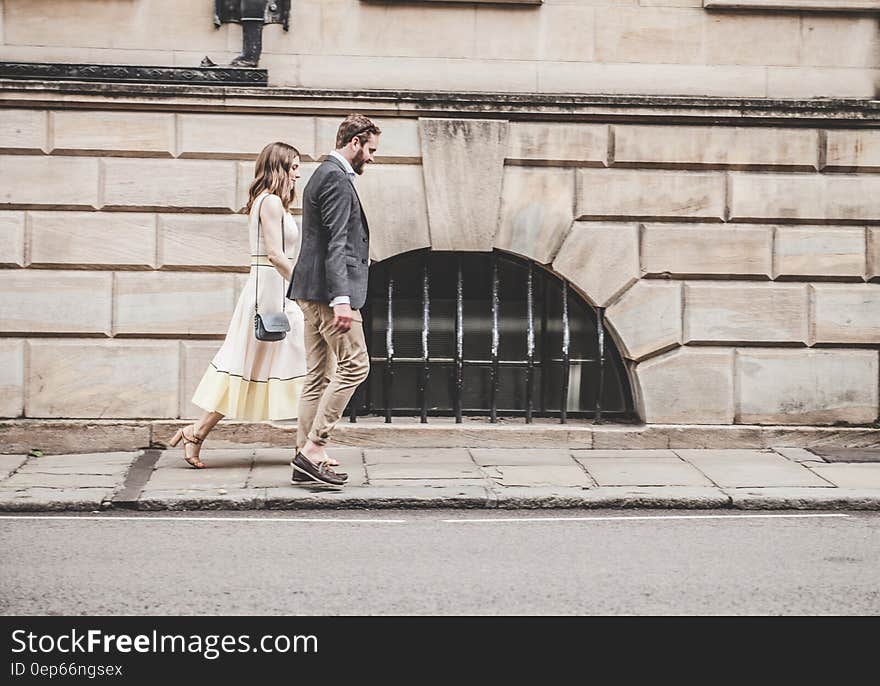 Man in Black Formal Suit Jacket Walking Together With Woman in White Sleeveless Dress