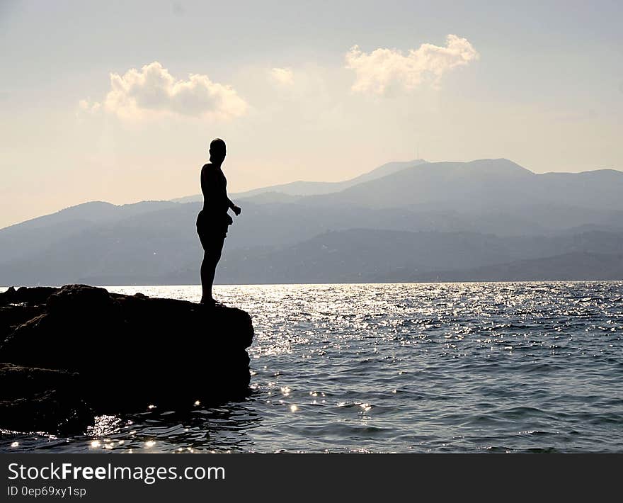 Person Standing on Rock Besides Sea Near Island during Daytime