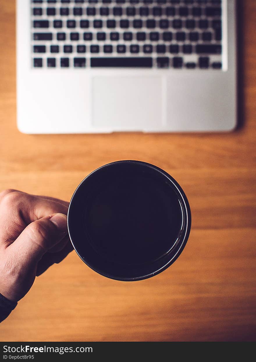 Hand holding mug of coffee over wooden desktop with laptop computer. Hand holding mug of coffee over wooden desktop with laptop computer