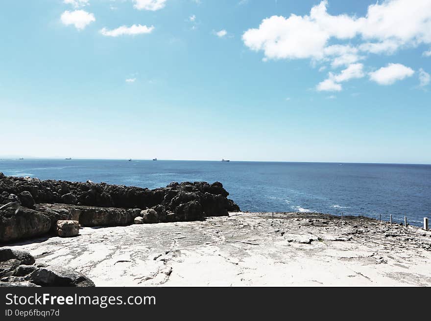 Piled Rocks Near Blue Sea Under Teal White Sky at Daytime