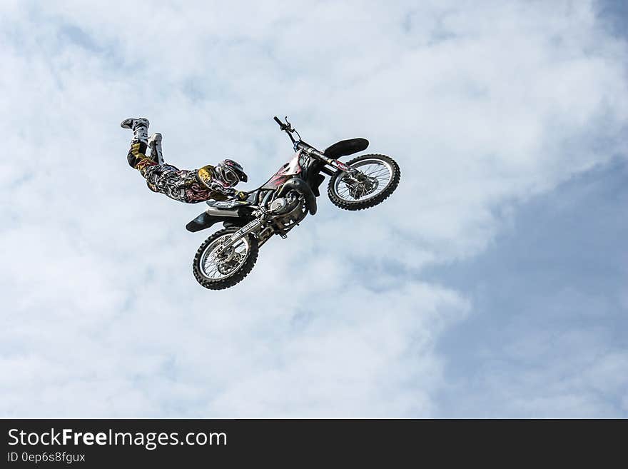 Motorbike stunt man flying through the air on a bike clinging only to the saddle, blue sky and cloud.