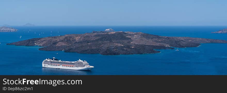 White Crewship Near Island Under Clear Sky at Daytime