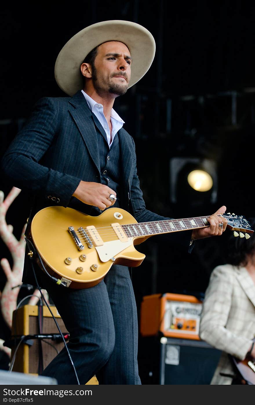 Man in Black and White Pinstripe Formal Coat and Pants Wearing Beige Hat Holding Brown Electric Guitar