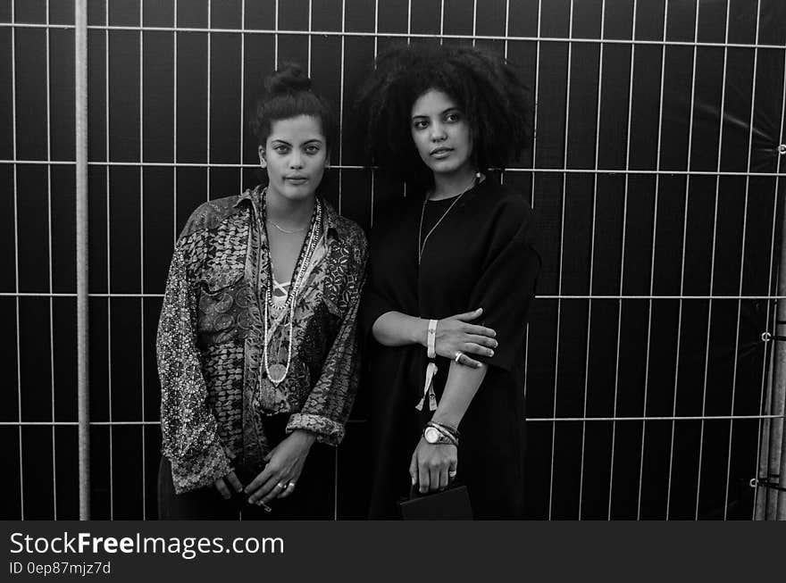 Greyscale Photo of 2 Woman Standing Behind Steel Bars