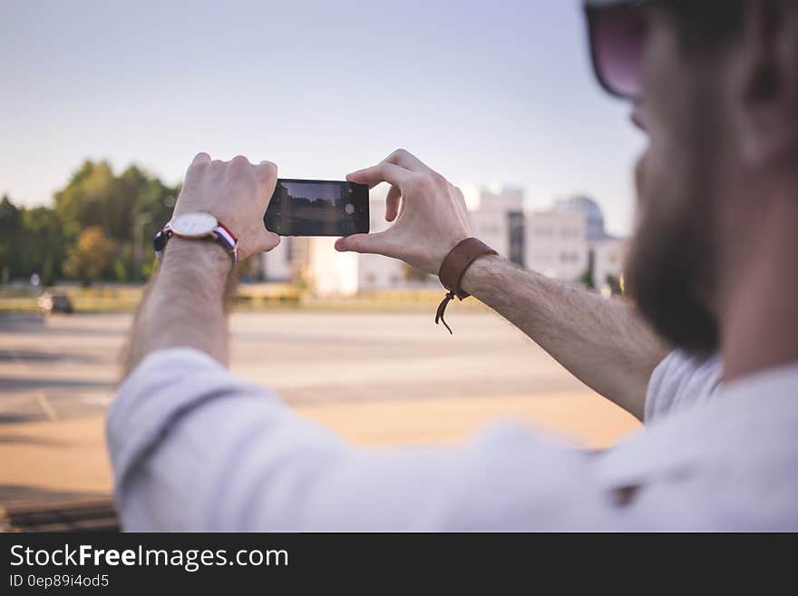 Tilt Shift Photo of Man Holding Black Smartphone Taking Photo of Gray Ground at Daytime