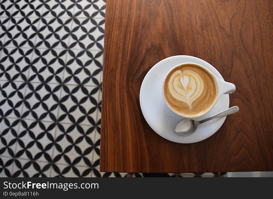 Overhead view of cup of cappuccino coffee on wooden table with decorative pattern.