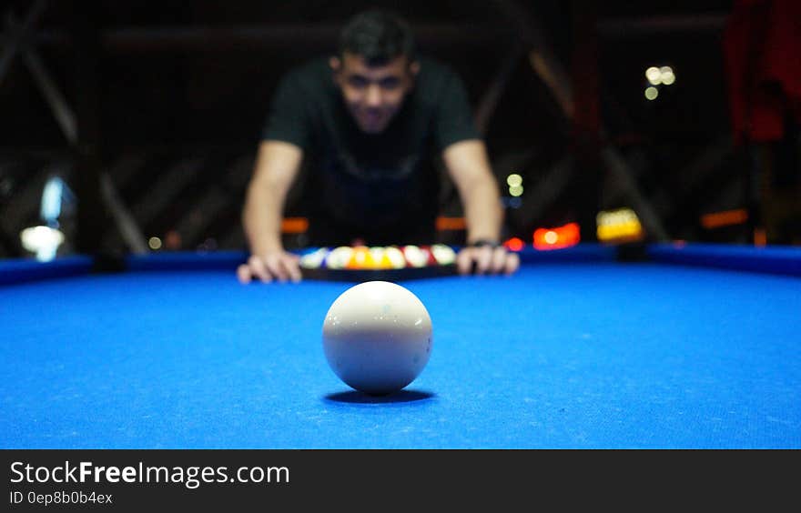Man using a triangle to set up pool balls on blue baize table with white ball on foreground. Man using a triangle to set up pool balls on blue baize table with white ball on foreground.