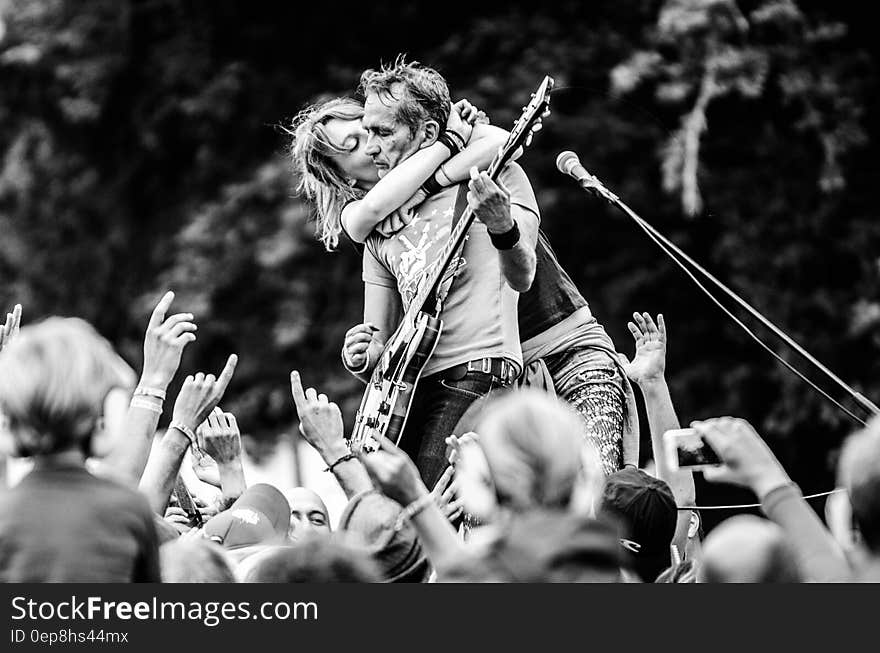 Grayscale Photo of a Woman Kissing a Man Playing Guitar