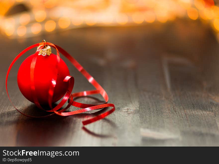 Red Christmas Bauble With Red Ribbon on Wooden Surface in Close Up Photography