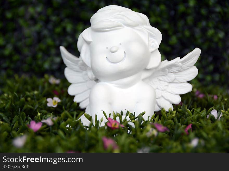 White Angel Ceramic Figurine on Green Grass With White and Purple Flower