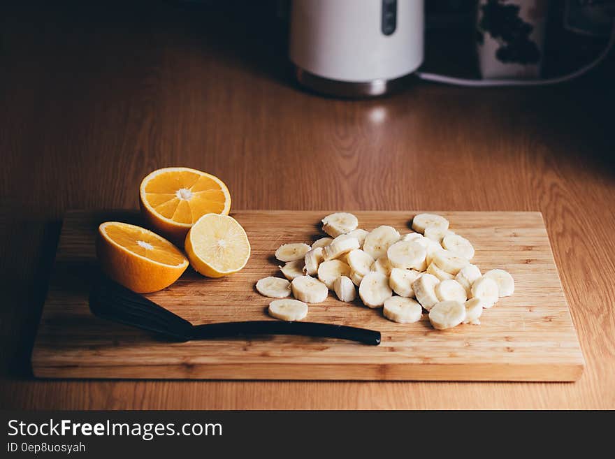 Sliced bananas and orange halves on wooden cutting board with utensil on kitchen counter. Sliced bananas and orange halves on wooden cutting board with utensil on kitchen counter.