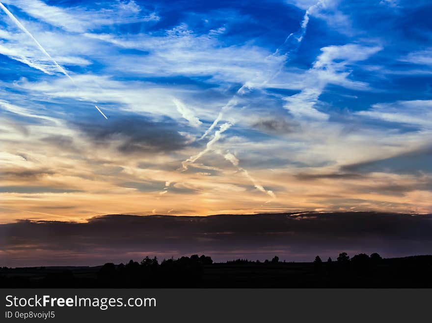 Golden dawn with forest plain and distant purple hills at dawn in golden light and blue sky above with vapor trails. Golden dawn with forest plain and distant purple hills at dawn in golden light and blue sky above with vapor trails.