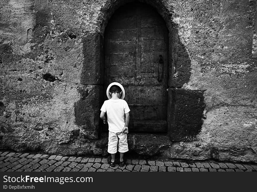 Grayscale Photo of Toddler Standing and Wearing Hat on the Ground