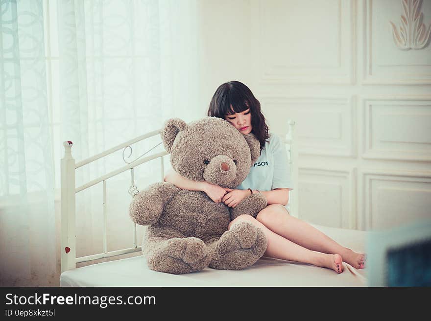 Portrait of beautiful Asian woman hugging teddy bear sitting on bed inside bedroom. Portrait of beautiful Asian woman hugging teddy bear sitting on bed inside bedroom.