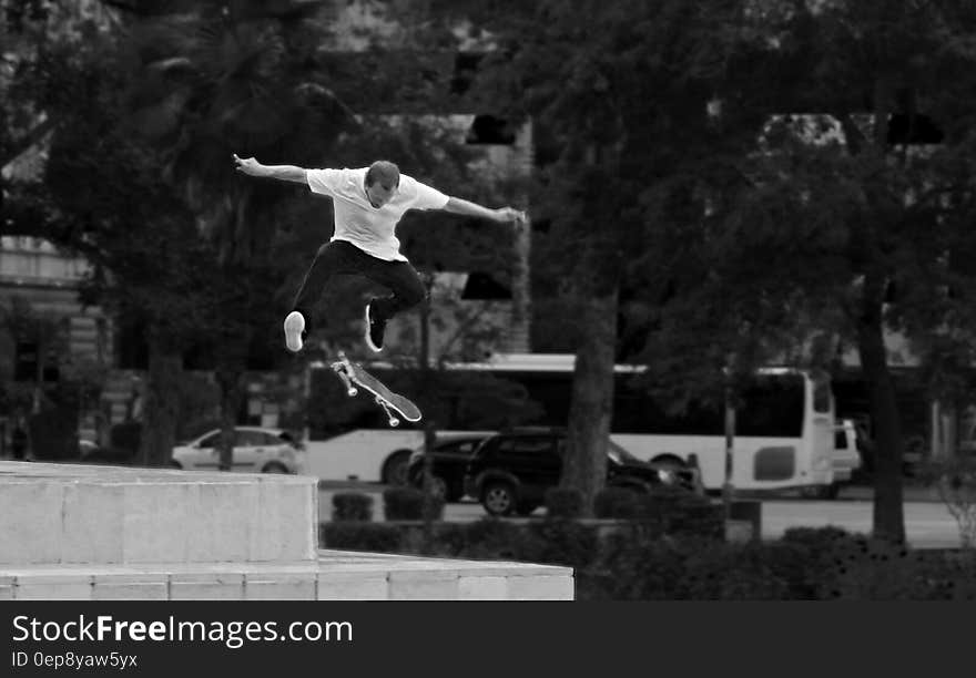 Man in White Shirt and Black Pants Playing Skateboard Near Green Tree during Daytime