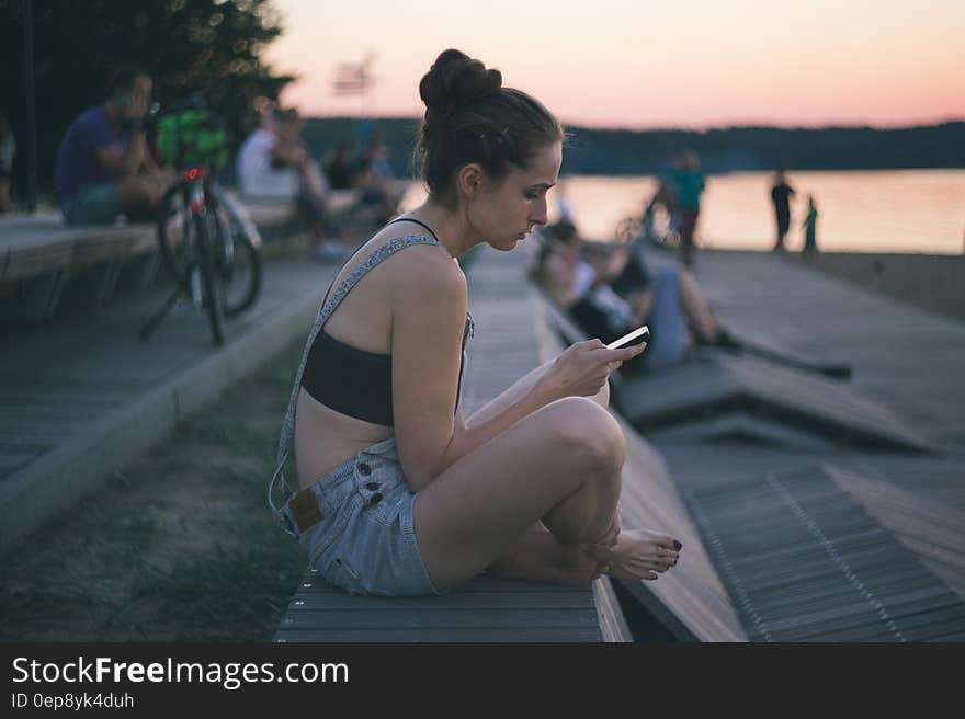 Woman in Black and Gray Shirt Sitting Near Ocean at Sunset