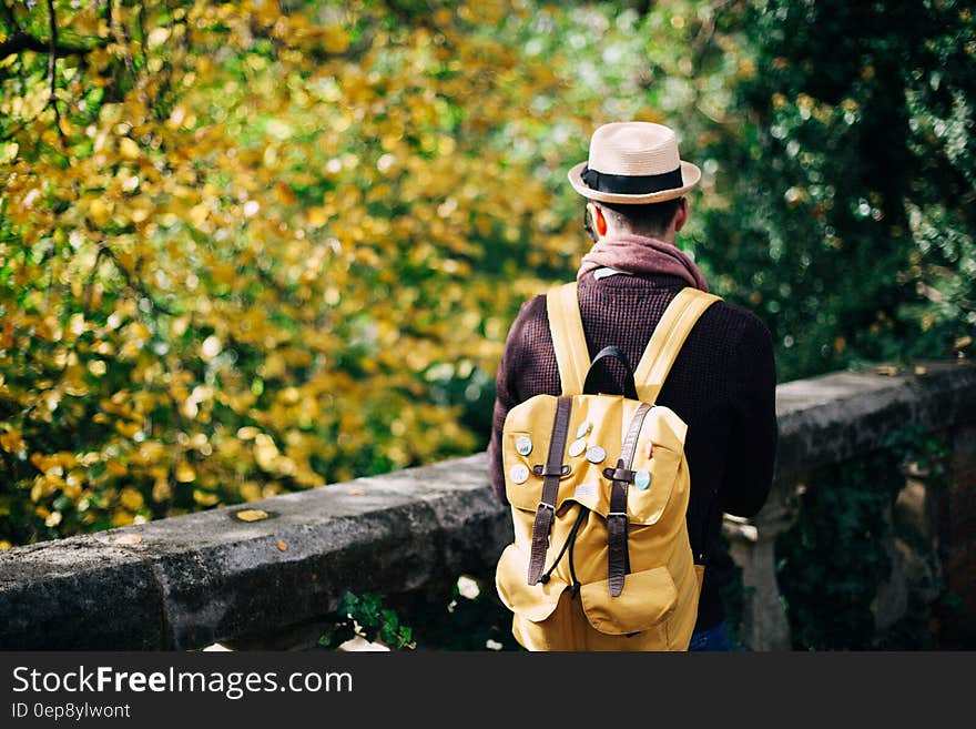 Man in White Fedora Hat and Beige Knapsack Beside Grey Concrete Railings during Daytime