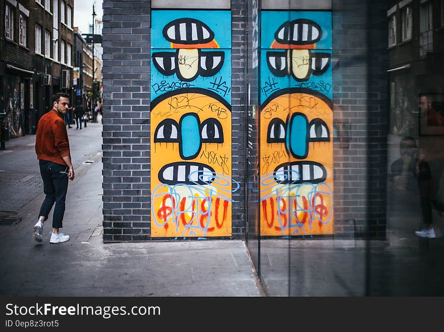 Person Wearing a Red Dress Shirt Walking Near a Wall Graffiti