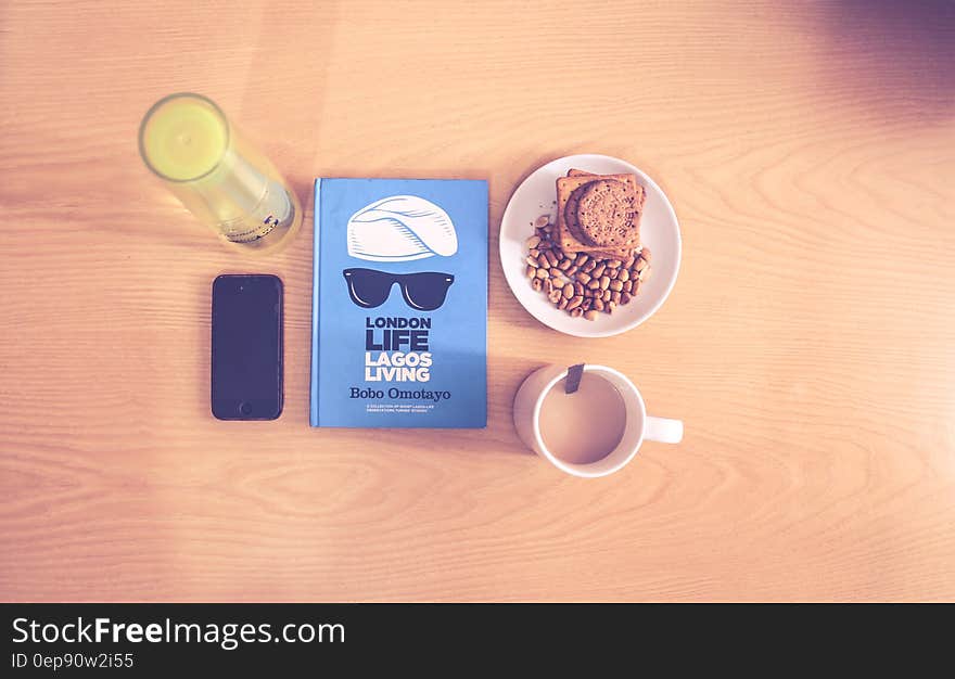 Space Gray Iphone Beside Blue Labeled Book Near White Ceramic Cup With Liquid Content