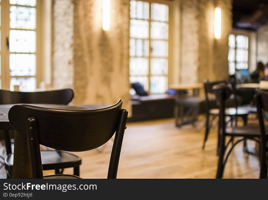 Black Wooden Tables and Chairs Arranged Inside Restaurant With Yellow Sconce