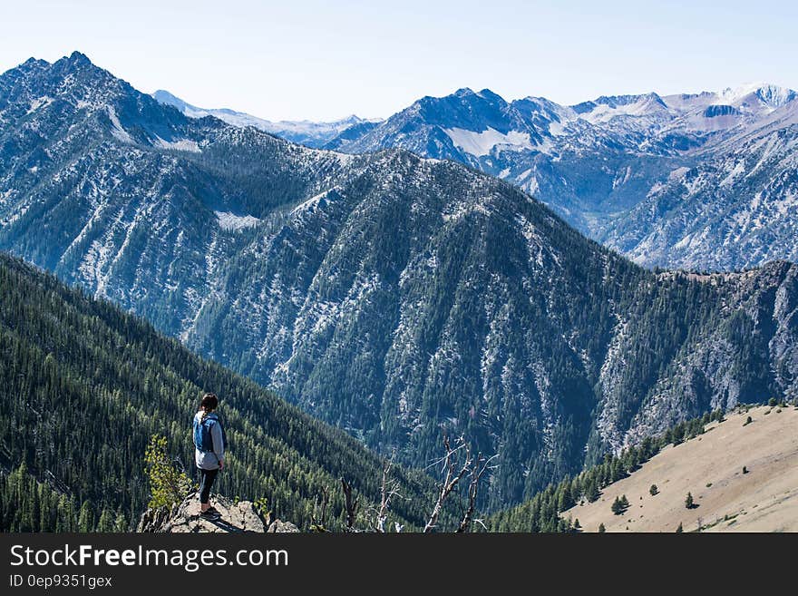 Hiker on mountain peak looking over valley forest.