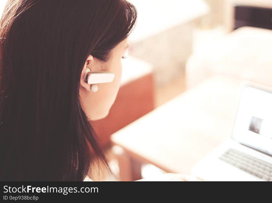 Woman Wearing Earpiece Using White Laptop Computer