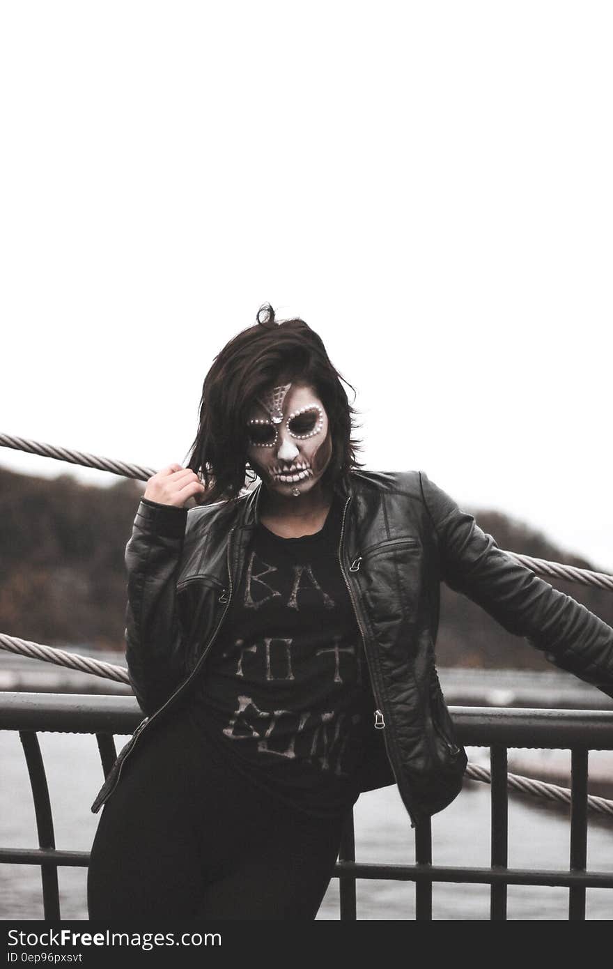 Woman Wearing Gray Halloween Mask and Black Leather Jacket Standing by Black Railings