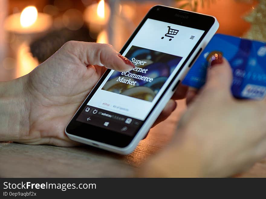 Person Using Black And White Smartphone and Holding Blue Card