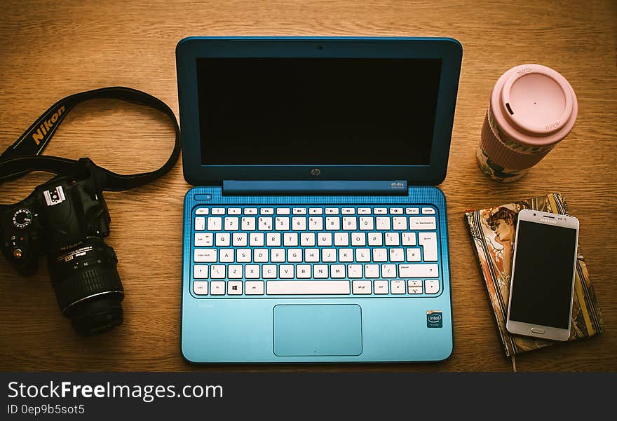 Blue Hp Netbook Beside Black Nikon Dslr Camera and White Samsung Smartphone on Book