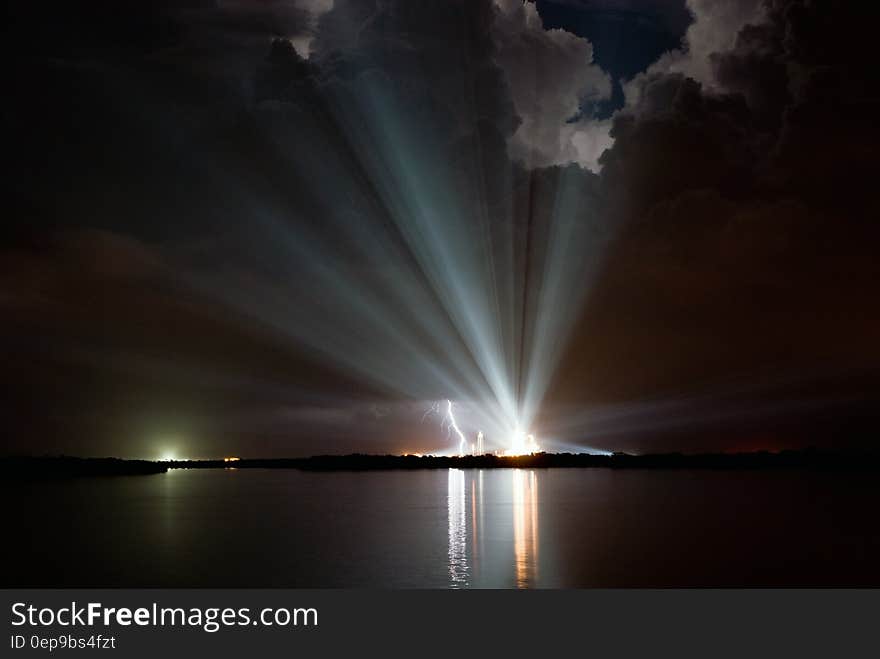 Lightening strike next to bright spotlight along waterfront in night skies. Lightening strike next to bright spotlight along waterfront in night skies.